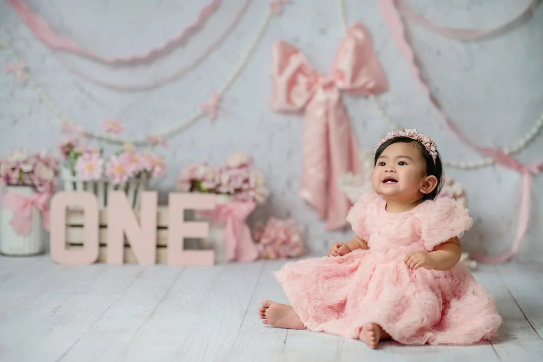 Baby in a pink dress beside ONE letters and a pink bow backdrop