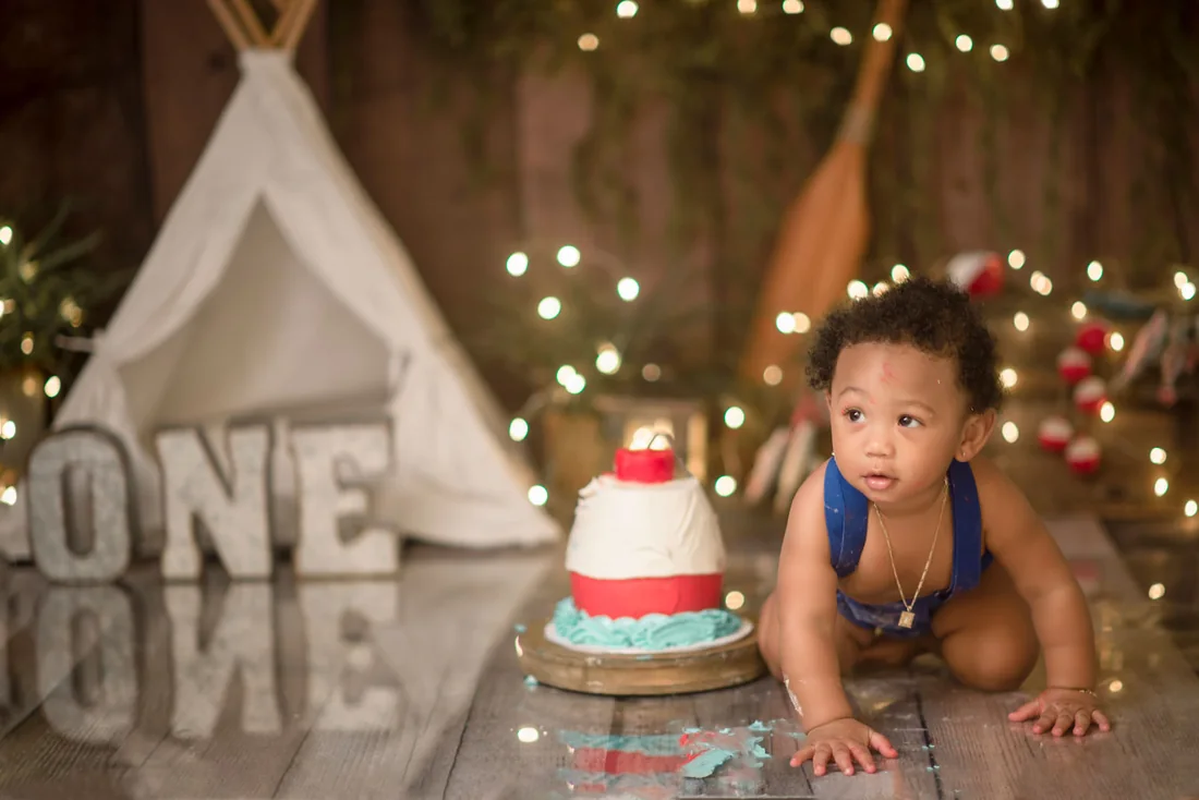 Birthday boy crawling beside his cake on a wooden studio floor