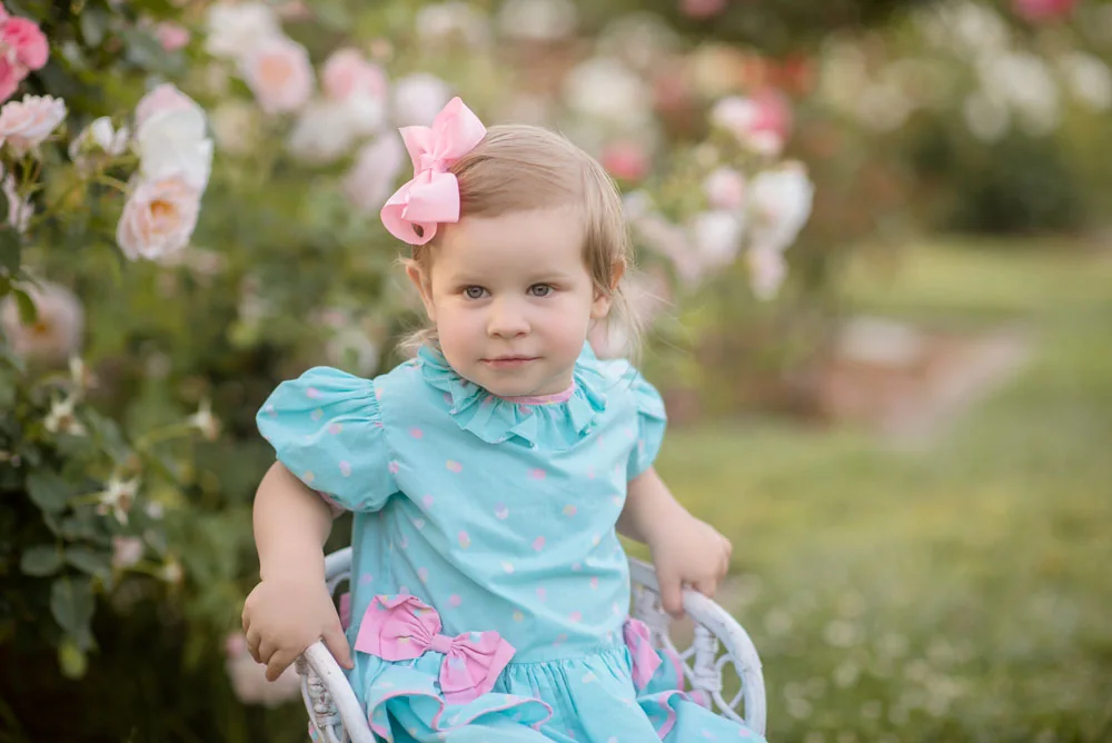 Close portrait of a girl wearing a pink bow in the rose garden