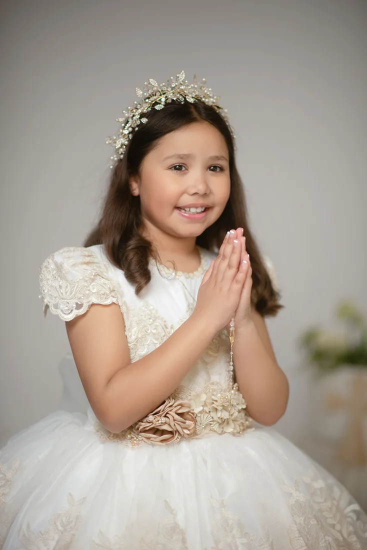 Girl in a white Communion dress with her hands joined