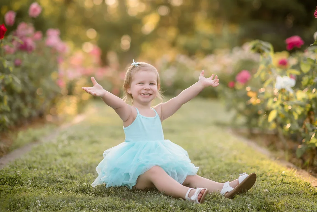 Girl raising her arms while sitting among the roses