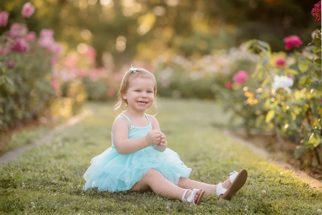 Smiling girl in a turquoise dress seated on the grass