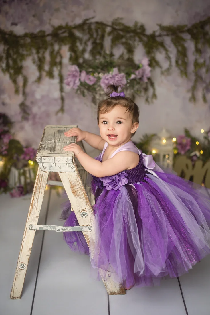 Stephanie smiling beside a small white ladder in her purple birthday dress