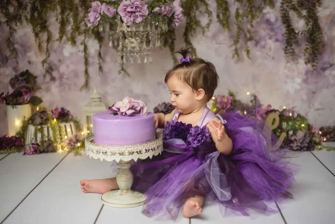 Stephanie reaching toward a purple birthday cake on a white stand