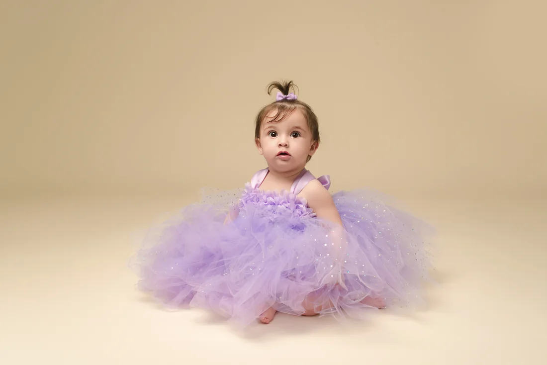 Stephanie sitting in a lavender tulle dress against a warm neutral backdrop