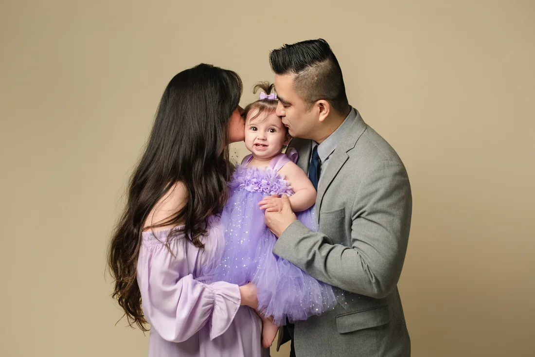 Parents kissing Stephanie on both cheeks during their family portrait