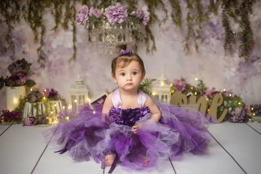 Stephanie sitting in a purple dress beneath flowers and greenery