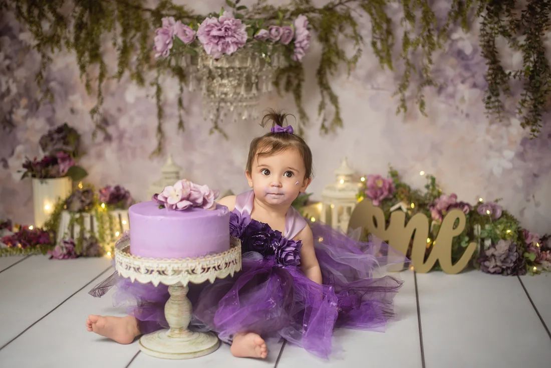 Stephanie smiling at the camera beside her first birthday cake