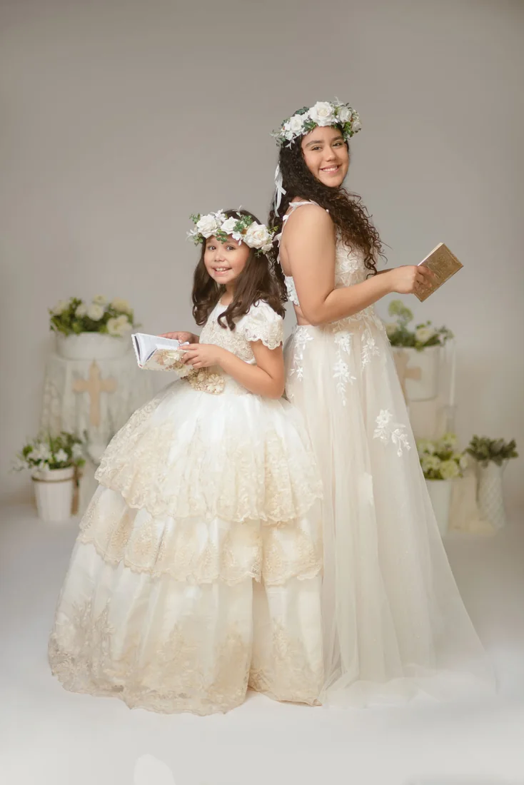 Two girls in white Communion dresses standing with books