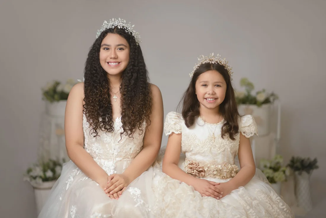 Two girls smiling together in white dresses and floral crowns